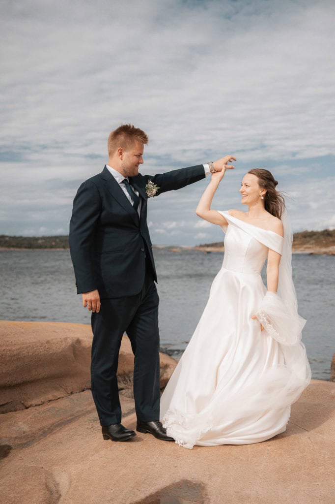 Nygifte par danser på stein ved sjøen under bryllup på Hvaler, med hav og skydekke i bakgrunnen.