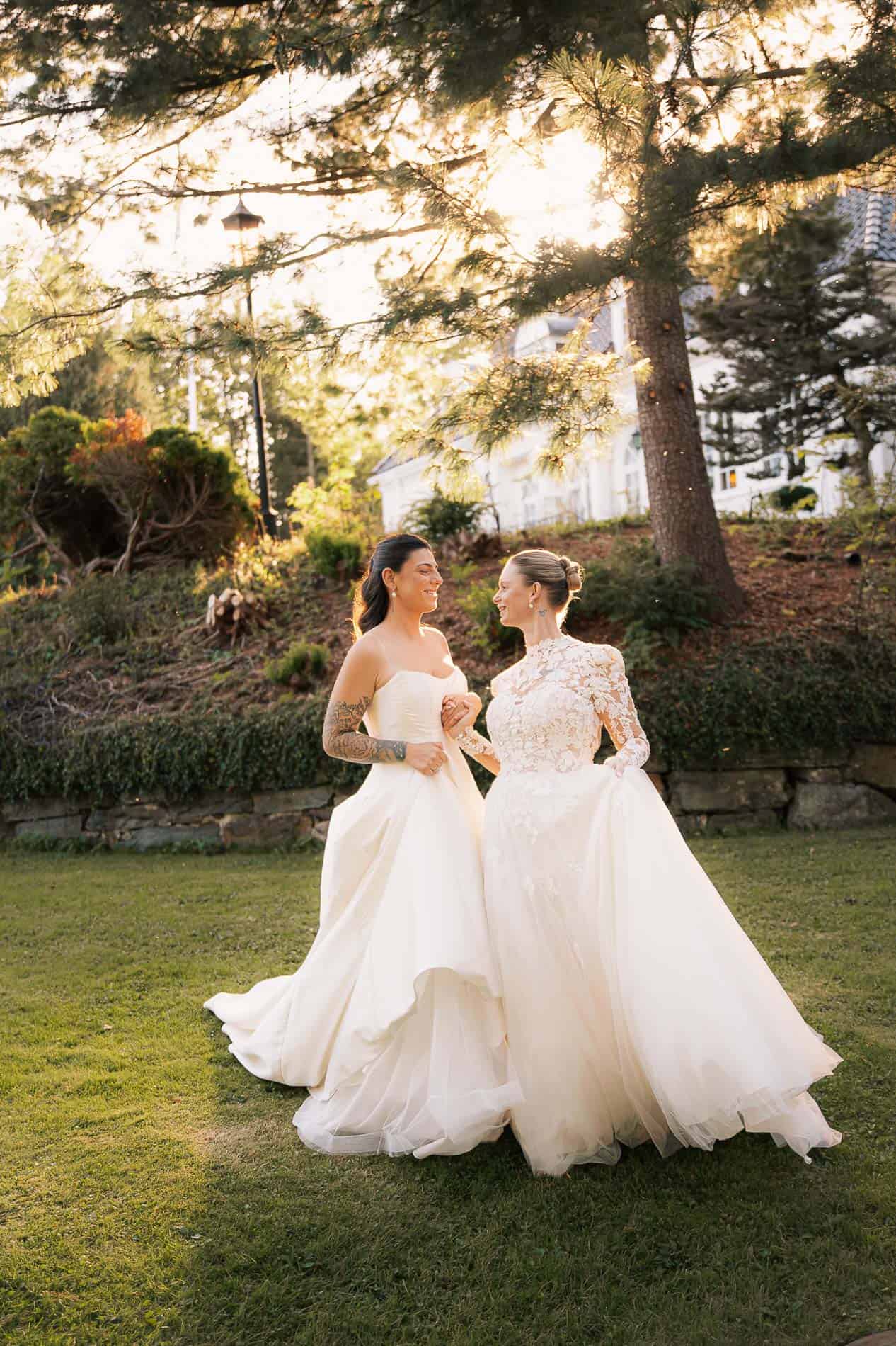 Bryllupsfoto av to kvinner i vakre brudekjoler i utendørs setting.