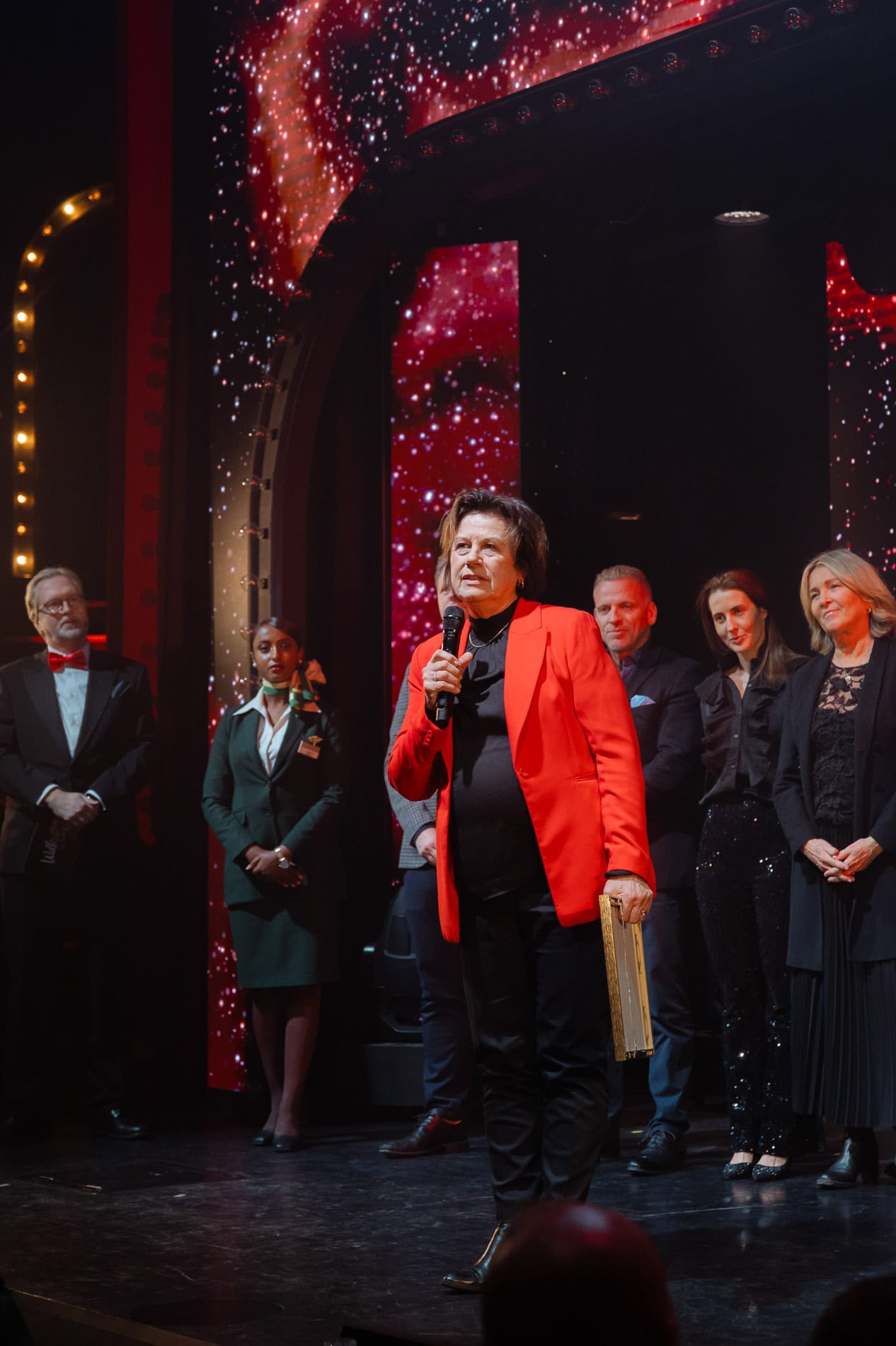 Heidi Henriksen holder tale under bedriftsarrangement, omgitt av forretningsfolk i formelle klær.