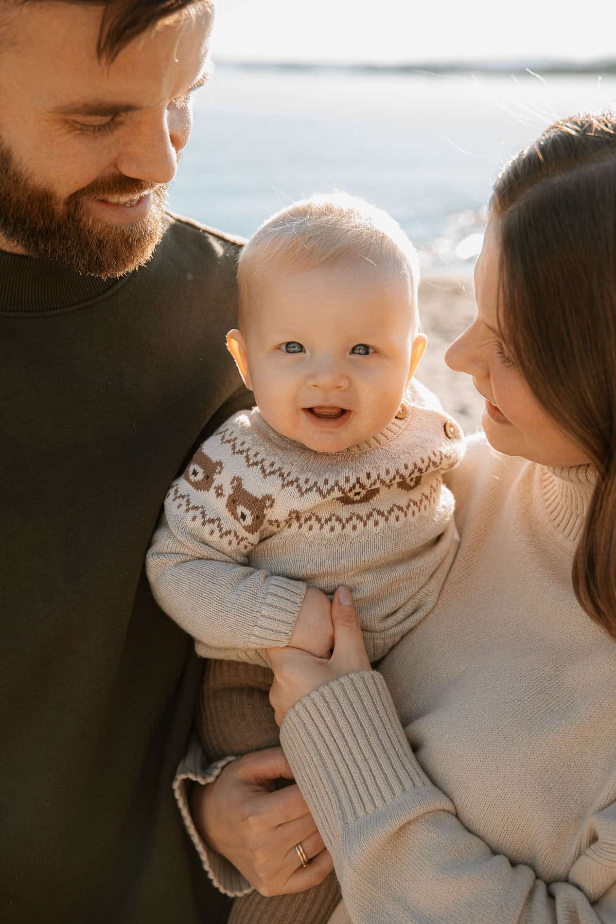 Familie med baby på stranden, smilende og nær hverandre.