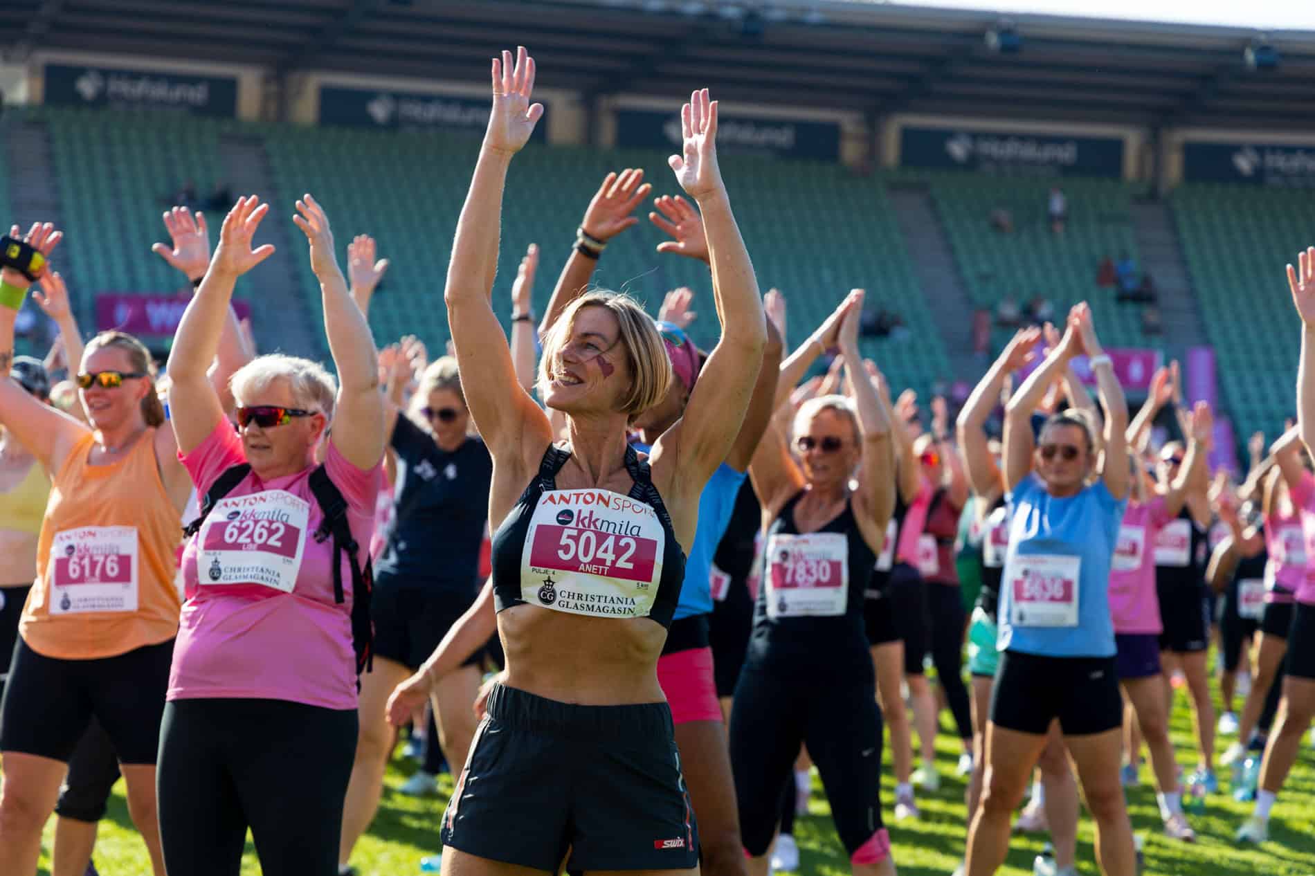 Gruppe kvinner som trener utendørs, smilende og løfter armene i en gruppeøvelse.