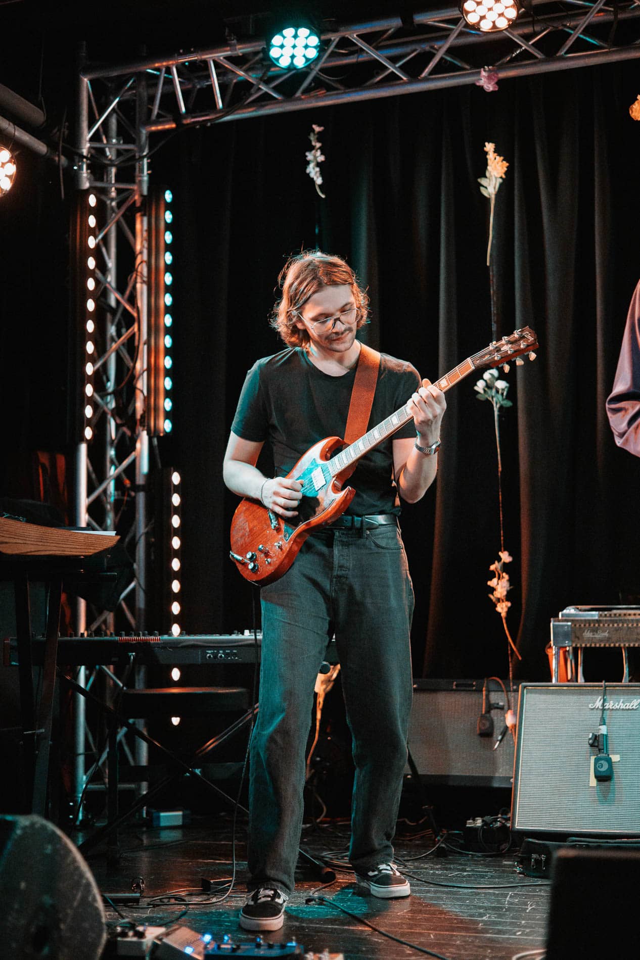 Kunstner med gitar under konsert på scenen, omgitt av scenelys og utstyr.