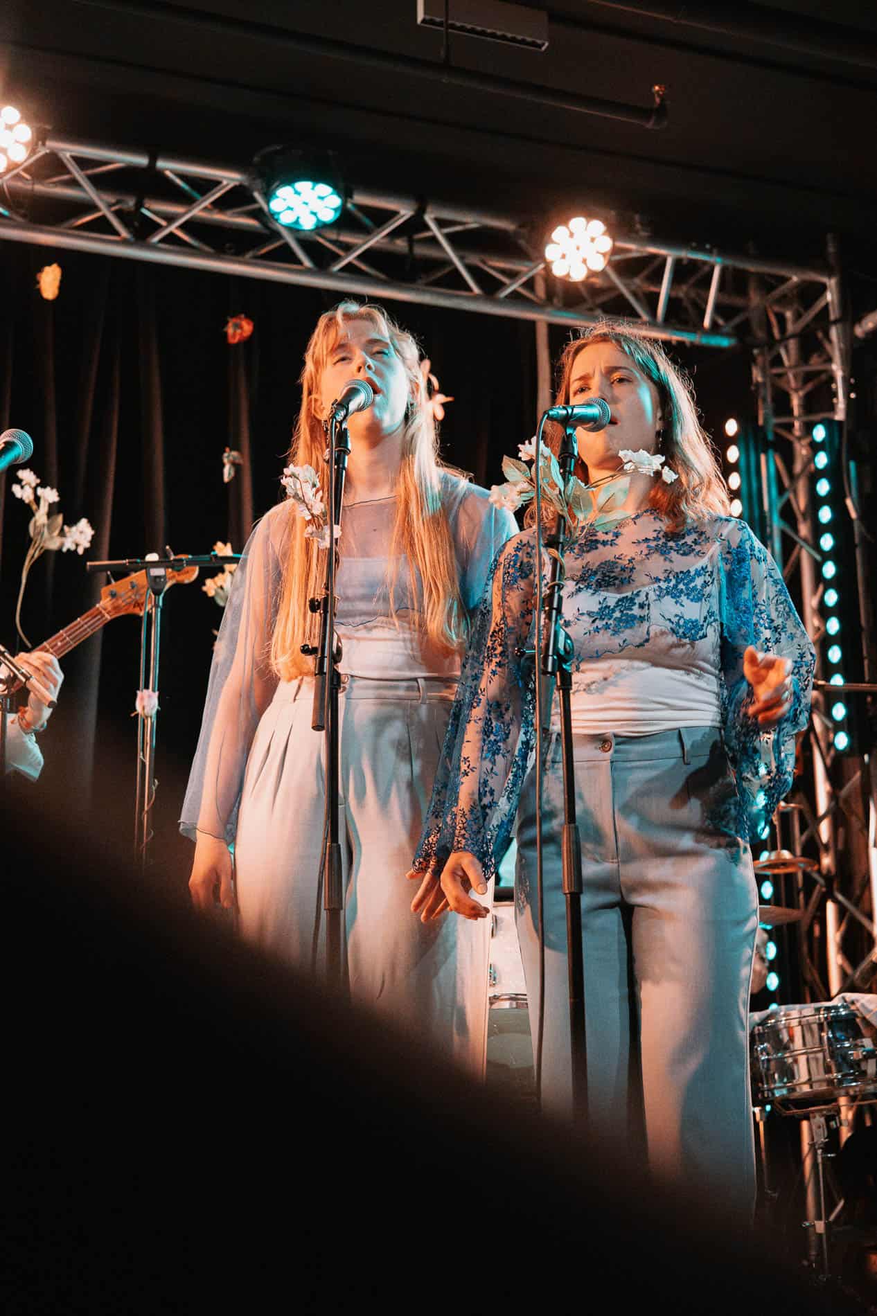 Kvinnelige artister synger på scenen med mikrofoner under en liveforestilling.