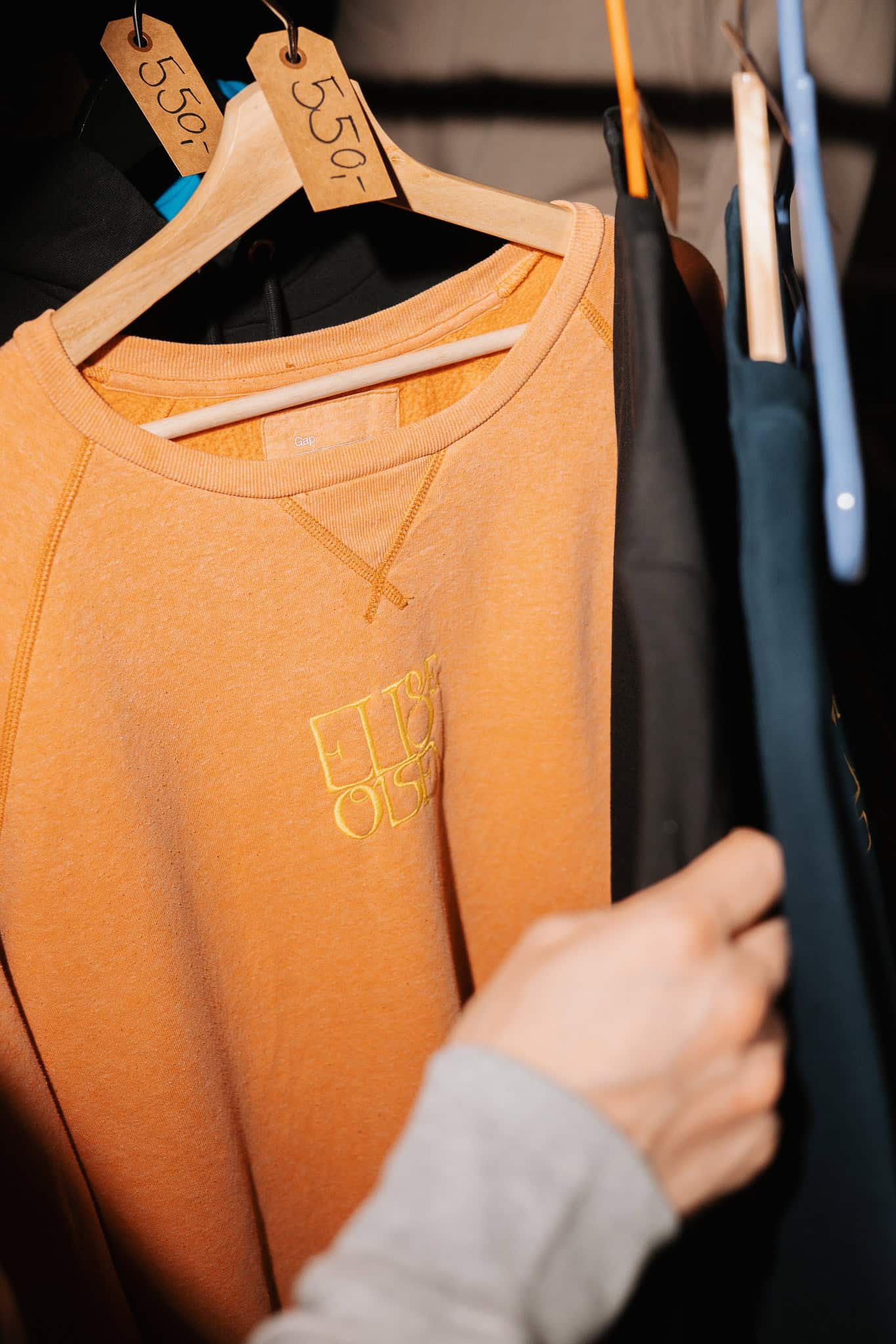 Oransje sweatshirt hengt opp på kleshenger i bedriftsfoto.