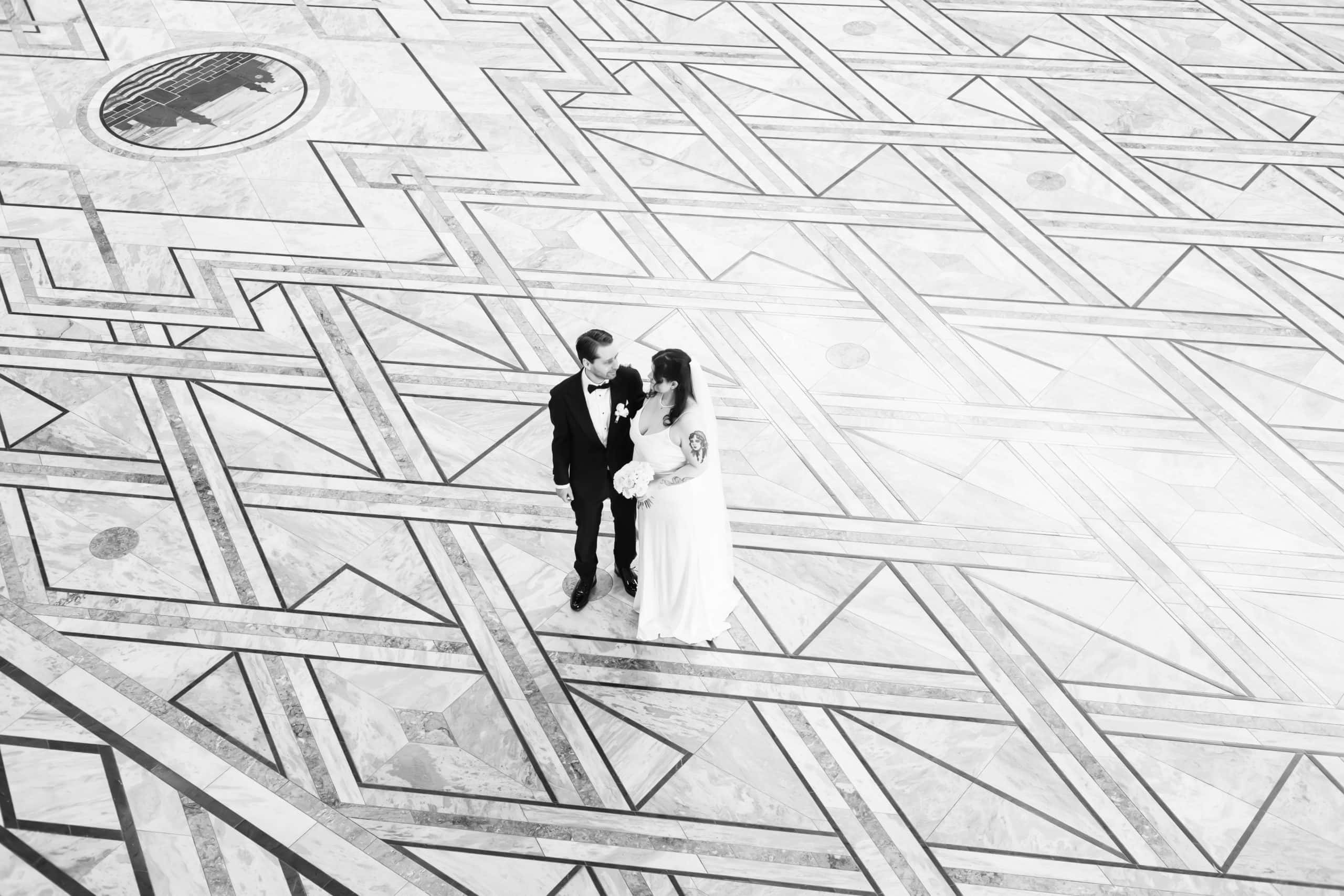 Elegant bryllupsfoto av et brudepar som står på et kunstnerisk mønstret gulv.