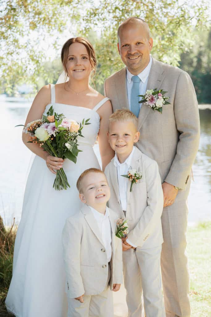 Familiebilde med foreldre og to barn i bryllupsantrekk ved vannet.