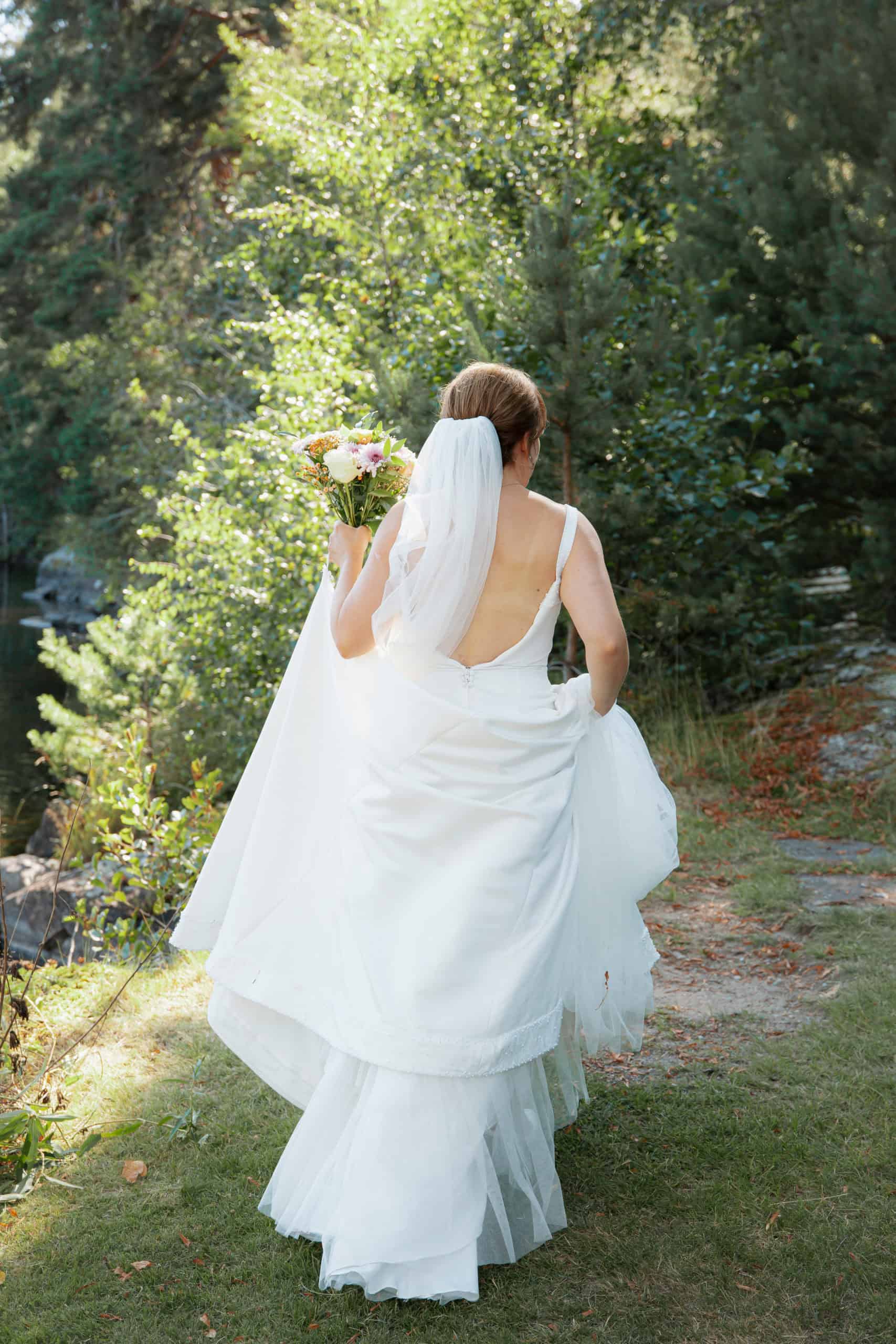 Brud i hvit kjole med blomsterbukett i skogen, portefølje.