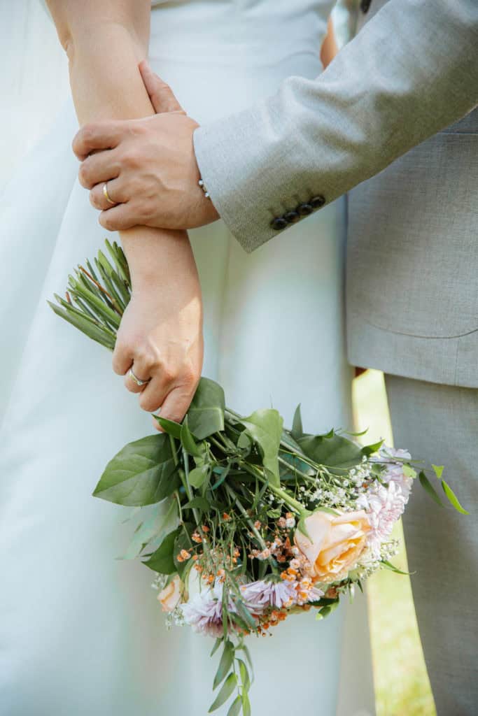 Nærbilde av brude- og brudgomshånd med blomsterbukett, portefølje av Heidi Henriksen.