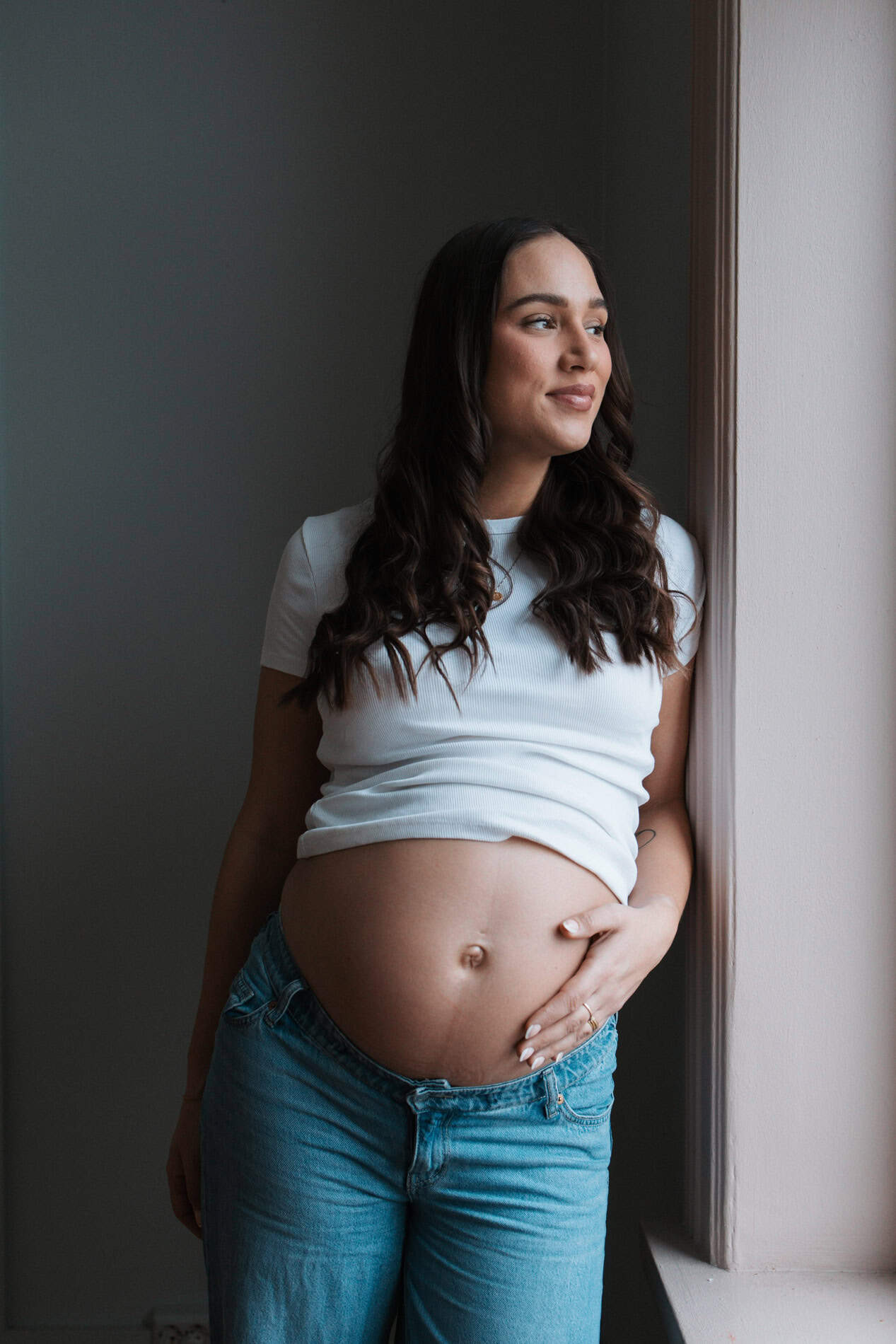 Gravid kvinne som nyter øyeblikket ved vinduet, fotografert av Heidi Henriksen.