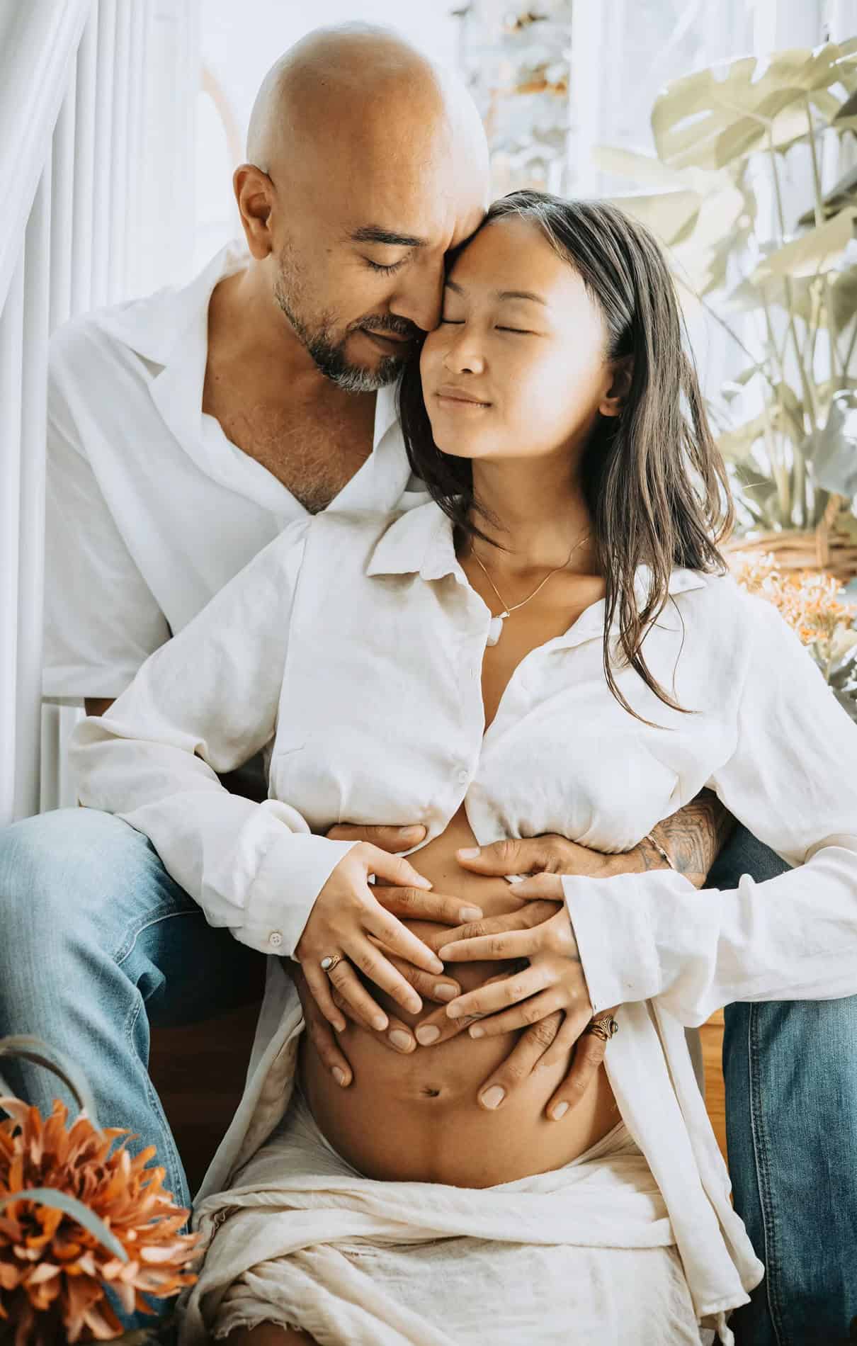 Familiefotografi av gravid kvinne med partner, intime øyeblikk hjemme.