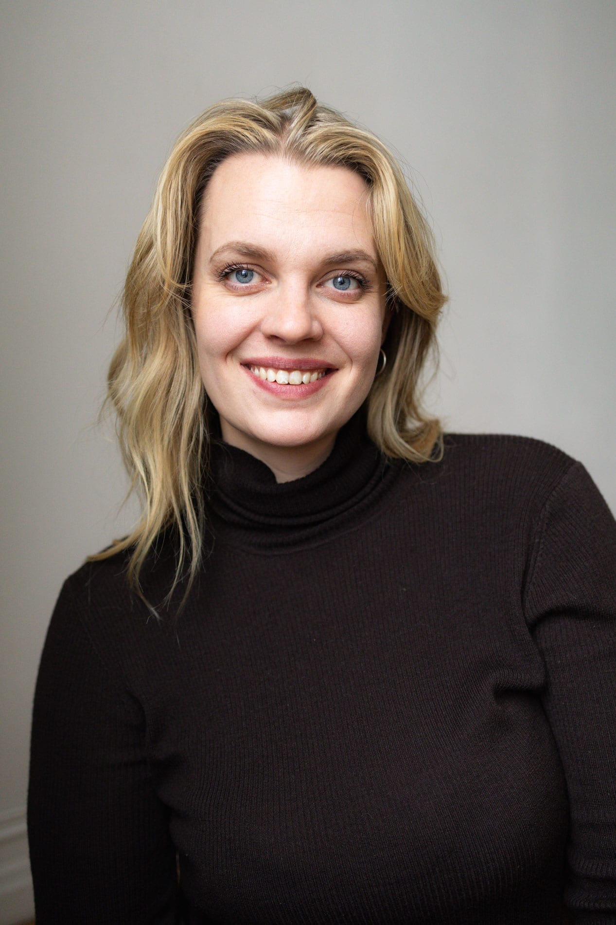 Heidi Henriksen smiler i studio, kledd i svart genser, med naturlig bakgrunn.