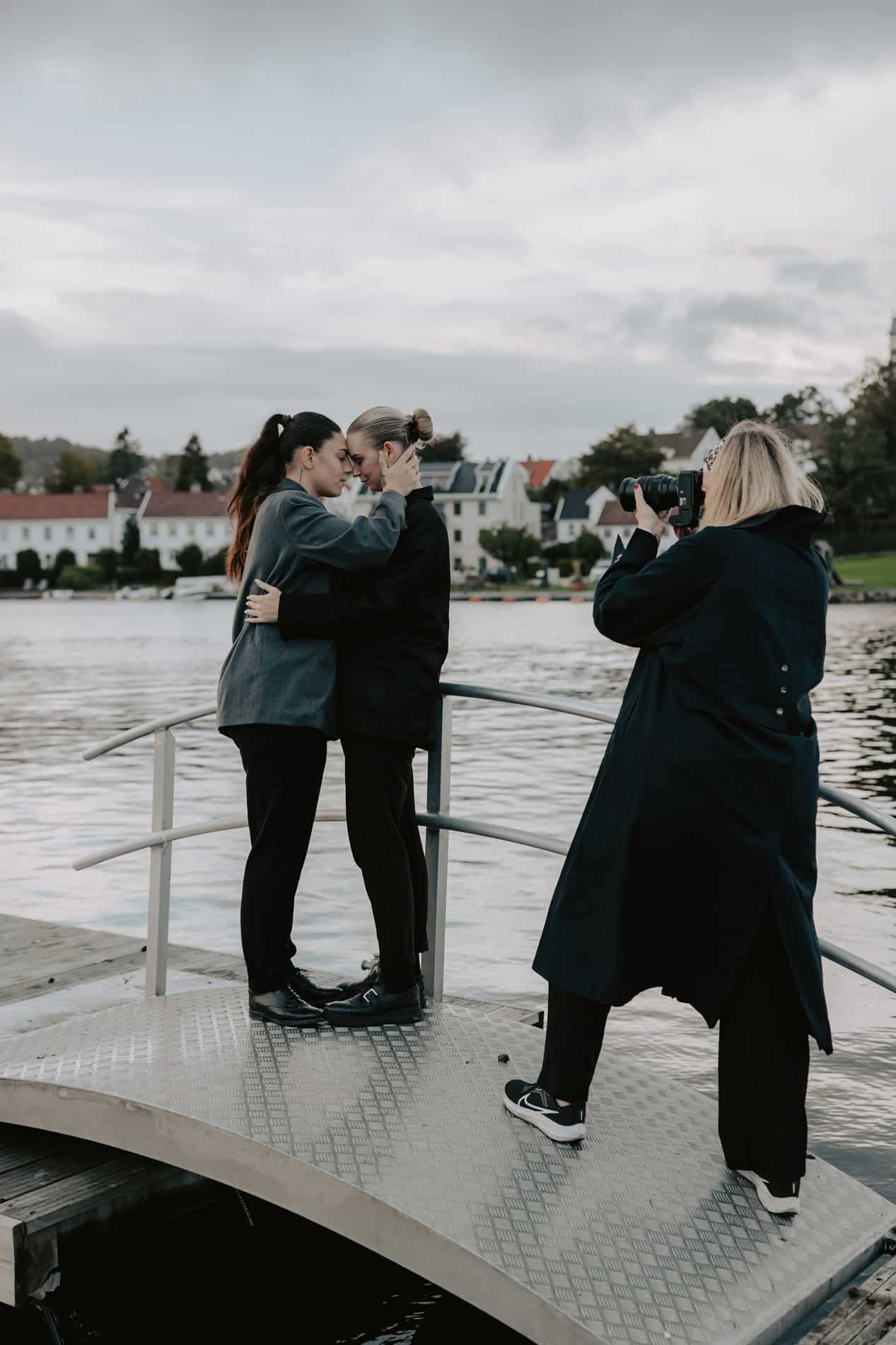 To personer kysser hverandre på en brygge med fotograf som tar bilder.